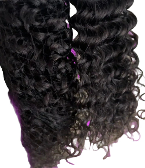 Two bundles of dark brown to black curly wig hair in a clear plastic bag, with a small pink and white tag visible on the left, against a plain beige background.